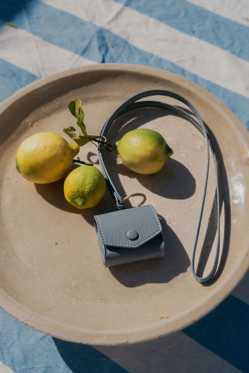 Airpods Hülle mit Schlüsselband in Ciel auf Teller mit Zitronen