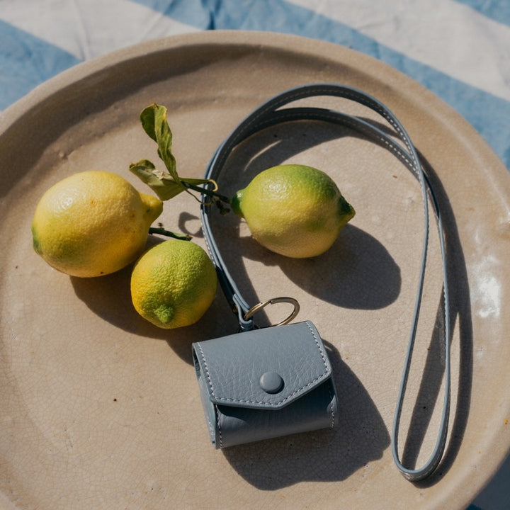 Hülle für Airpods an Schlüsselband in Ciel auf Teller mit Zitronen