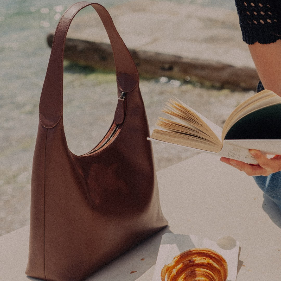 Hobo Schultertasche in Cinnamon Braun am Strand beim Buchlesen
