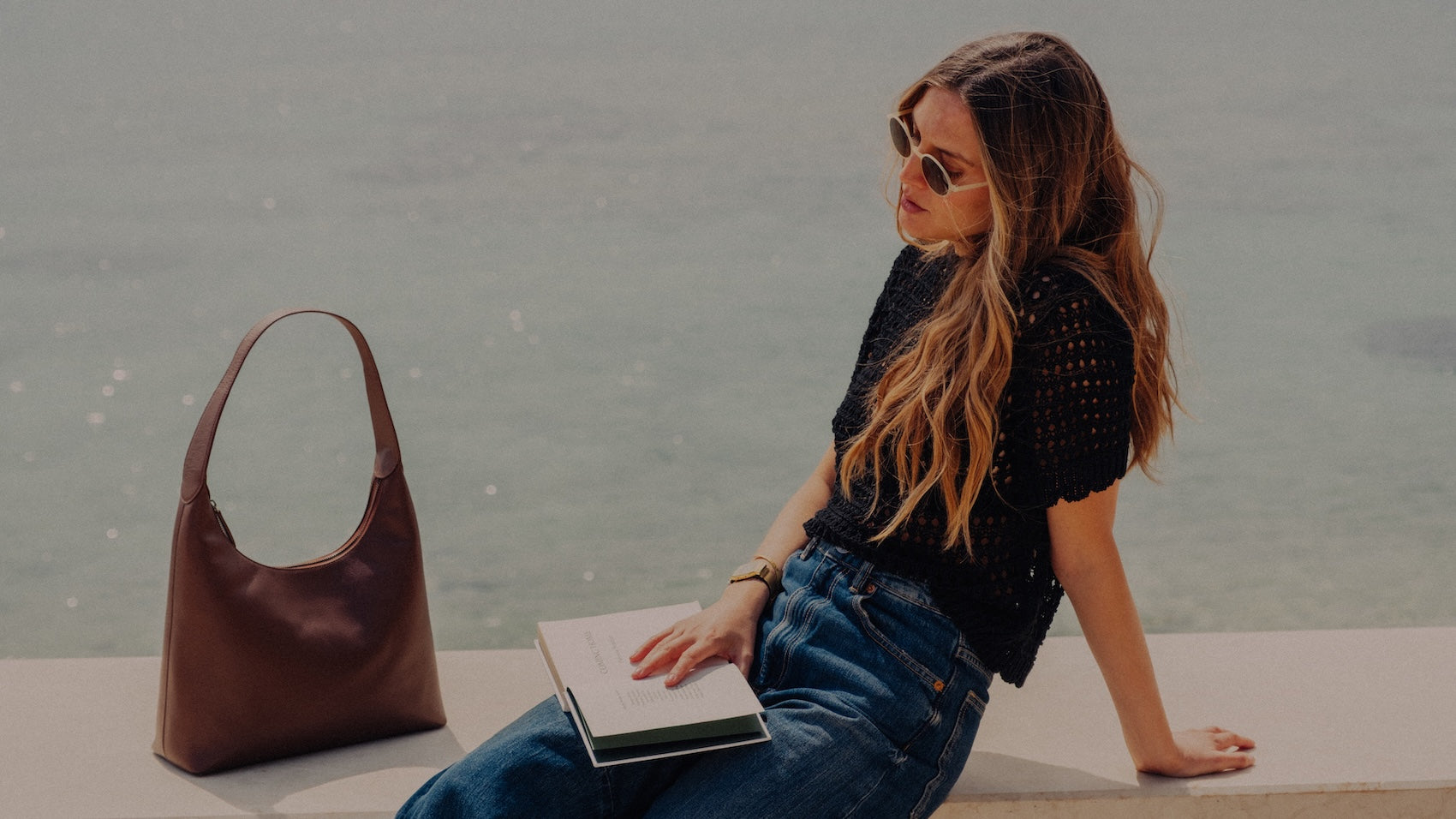 Schultertasche Hobo in Cinnamon Braun neben lesender Frau am Meer